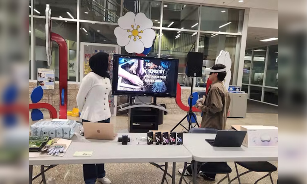 Two students stand at a table set up in Building 8 beside the metal flower sculptures.