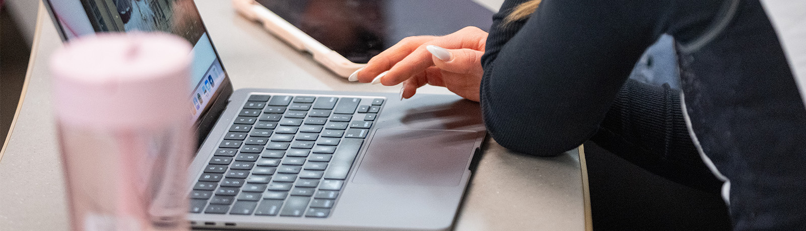 A student's hand hovers over the track pad of a laptop