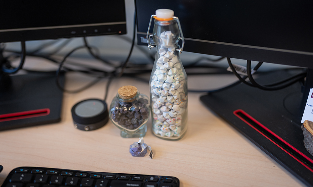 two jars, one shaped like a heart, stoppered with corks are filled with many tiny origami stars