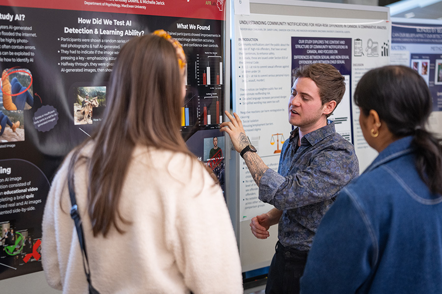 A student points at his poster while explaining his research to attendees