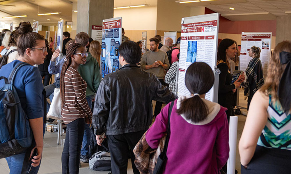 Students gather in front of posters at Student Research Day