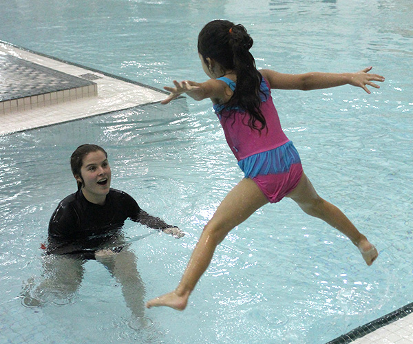 young girl jumping into swimming pool