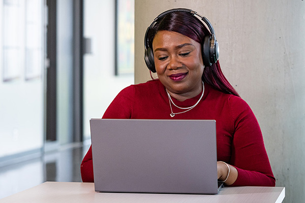 woman sitting at desk wearing headphones while on her laptop