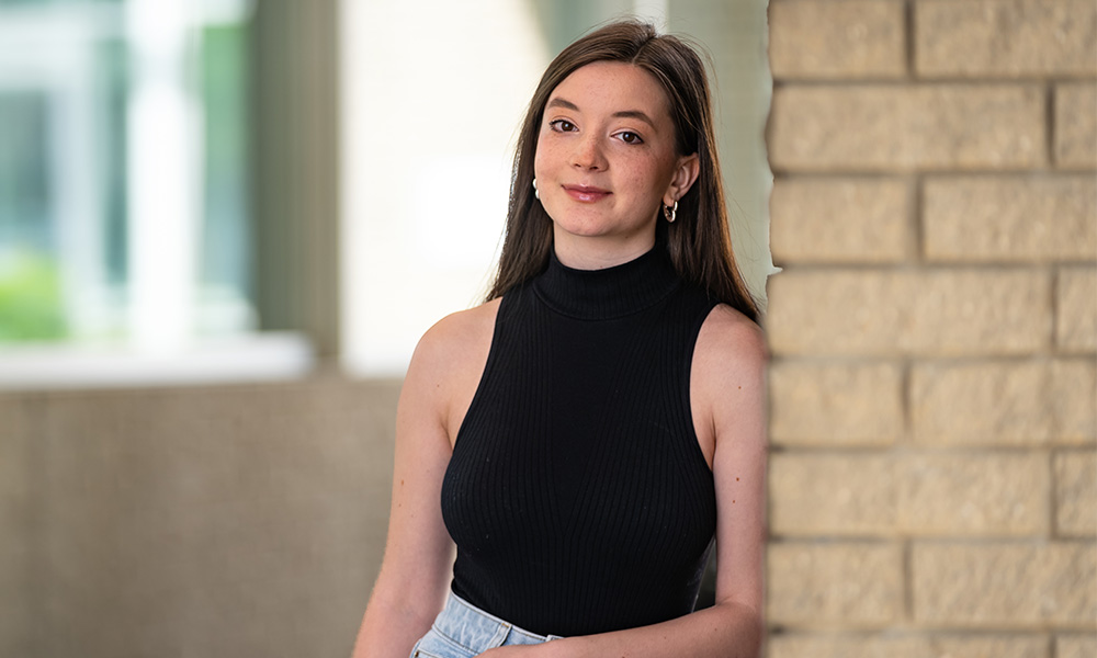 Kateryna Kuzmuk stands beside a brick column on MacEwan's campus.
