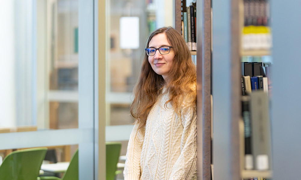 Ashley Platz leans against a bookshelf in the MacEwan Library
