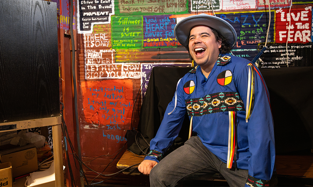 Josh Languedoc in front of a wall covered with hand-painted quotations by students.