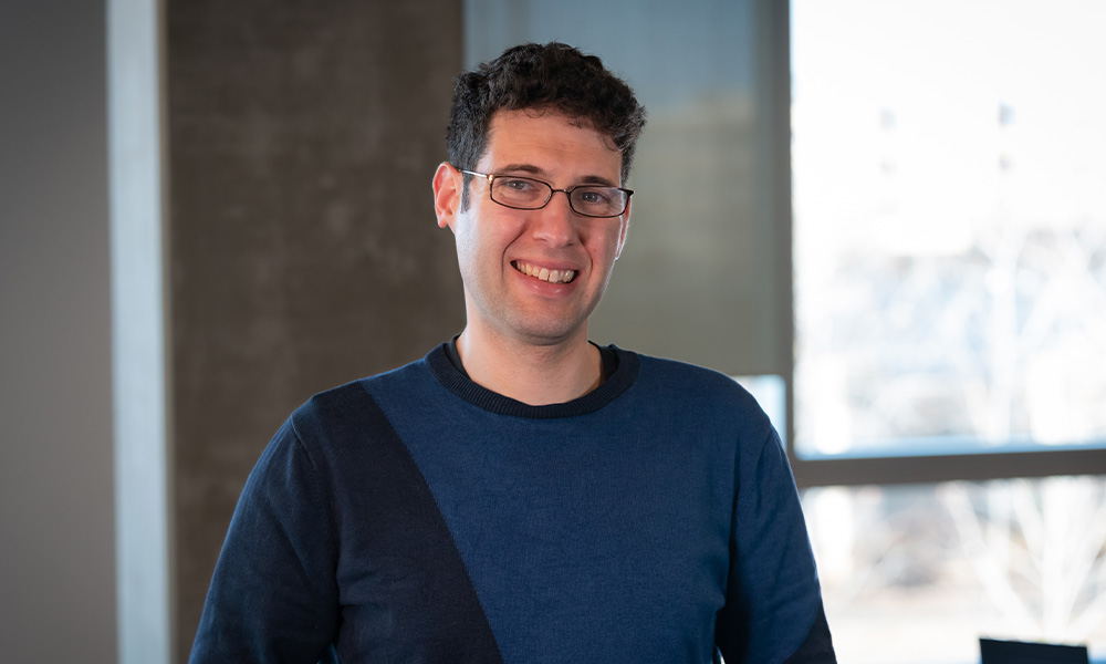 Dr. Miller wears a blue shirt and glasses and smiles