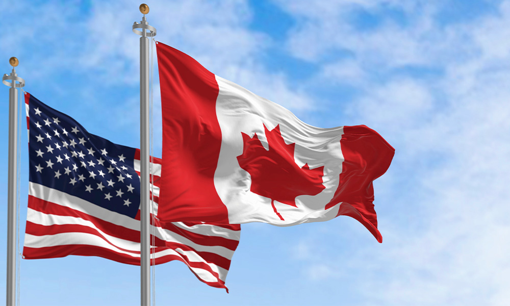 An American and a Canadian flag on flagpoles, side-by-side.