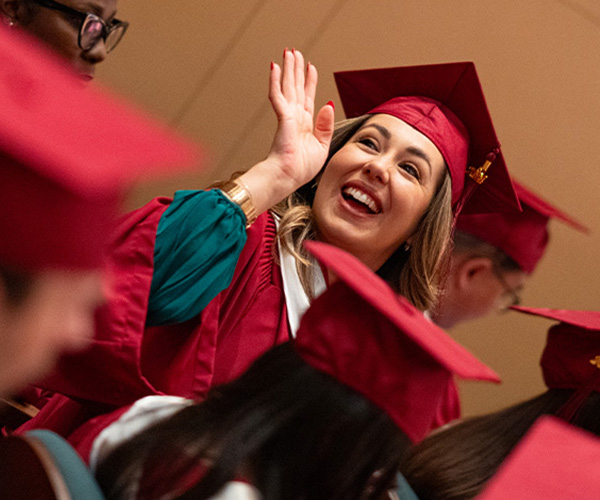 A grad waves while wearing a red cap and gown