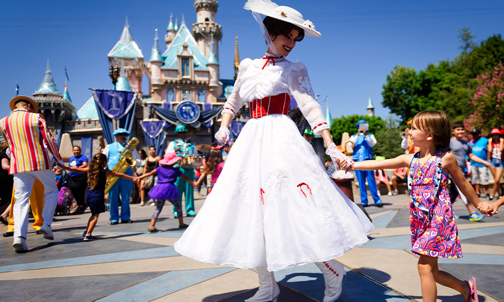 A woman in an elaborate costume holds hands with a small child while a band plays in the background.