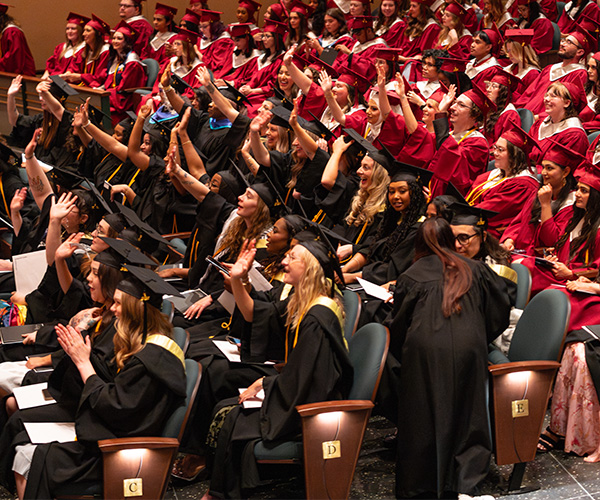 People in caps and gowns smile and wave toward the stage in the Winspear Centre.