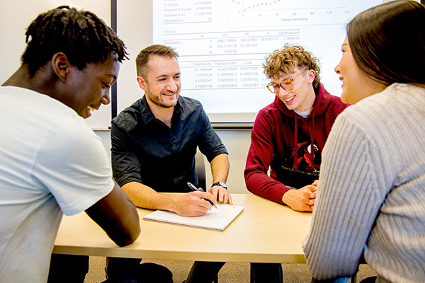 group of students sitting around a desk talking to a teacher