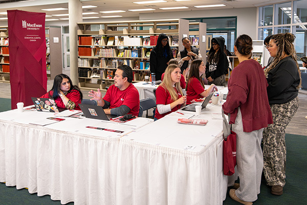 students in the library speaking to volunteers about applications