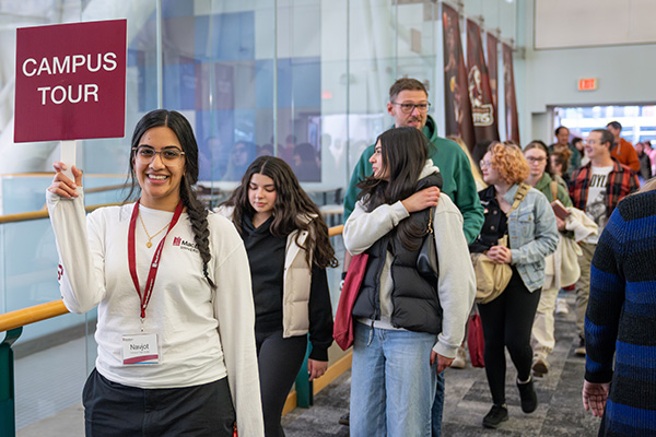 MacEwan volunteer walking with campus tour sign and people walking behind her