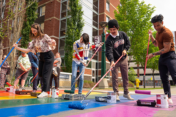 students painting a rainbow sidewalk outdoors