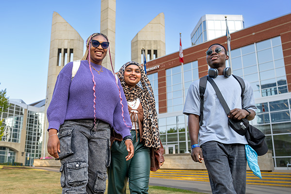 three students walking outside on campus with MacEwan University in the background