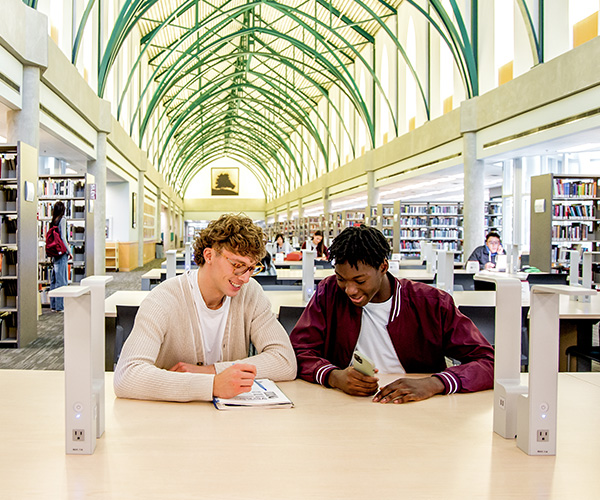 two male students sitting in a library working on school work