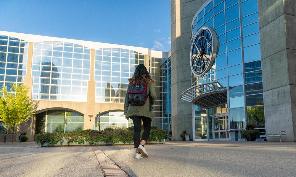 student with backpack walking into MacEwan building
